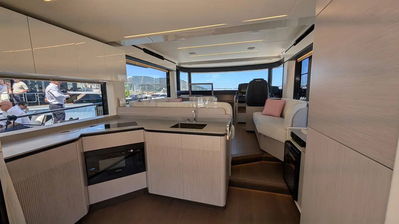 Modern yacht interior featuring a kitchen area, seating, and large windows showing a marina view.